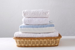 Stack of fresh clean towels in the wicker basket on the white table against bright wall