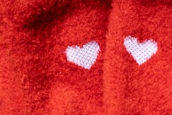 Closeup of two white knitted shapes of heart on the red socks.Empty space