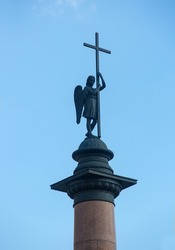 Bronze sculpture of an angel with a large cross on top of a red granite column