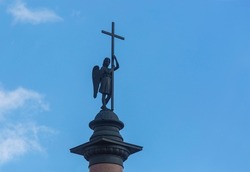 Bronze sculpture of a winged angel with a large cross on top of a red granite column