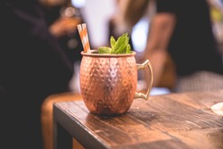 Close up on a copper cup with Moscow Mule cocktail, fresh mint as decoration and a white and orange carton straw
