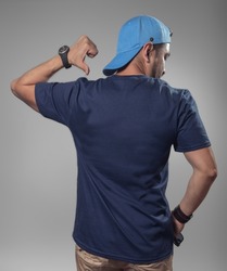 Back view of man. Mockup of male latin hispanic model wearing a navy blue t-shirt and blue cap pointing the back of his t-shirt on clear gray gradient background.