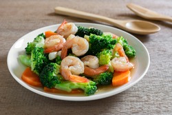 close up of stir fried broccoli with shrimps in a ceramic dish on wooden table. homemade style food concept.