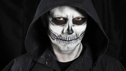 Halloween costume. Man with skeleton make-up. The man looks into the camera. Dark background. 