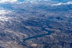 Aerial View of Idaho mountains and snake river from the sky while inside an airplane. View of brown mountains and trees covered with snow