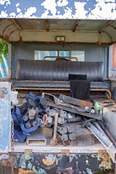 The back of an old dilapidated car filled with chairs and junk left in a yard