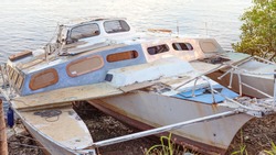 A decrepit damaged old wooden catamaran abandoned in a state of disrepair run ashore on a mangrove river bank