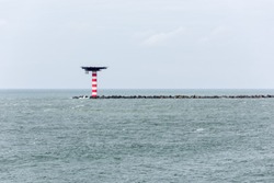 The red and white striped lighthouse with heliplatform at the entrance of the Port of Rotterdam in the Netherlands. The lighthouse is situated at the end of a pier with concrete wave breakers.