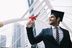Handsome businessman wear graduation degree hat and stand on stair near cityscape, business education concept