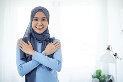 Embrace equity on multiracial Internal Women's Day. Muslim Asian woman good mood hands hug herself shoulders enjoy joyful blue cloth