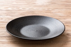 Perspective view of empty black plate on wooden background. Empty space for your design.