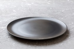 Perspective view of empty black plate on cement background. Empty space for your design.