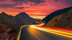highway view at sunset. car lights form long colored lines on the highway. road view through mountains and colorful sunset view. European highways and mountains. Bavaria, Germany.