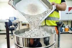 On site road testing laboratory. Placing sample of gravel into a silver container. Preparation step - pouring sample of a layer of soil  
