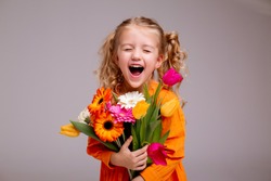 portrait of a little blonde girl with a bouquet of spring flowers on a light background. child in orange dress holding a bouquet of tulips in his hands. space for text. spring concept