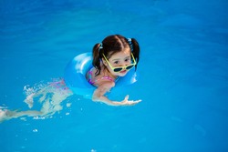happy little girl swims in the pool in summer in sunglasses, space for text
