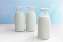 Three glass bottle of milk on the white table on a blue background. with copy space for text.