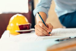 engineers holding a pen pointing to a building and  drawing outlay construction plan as guide for builders with details. Engineer design and writing blueprint.