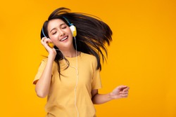 Happy young asian woman listening music in headphones and dancing on yellow background. Charming girl get fun and enjoying life. Attractive female enjoying her favorite song. copy space