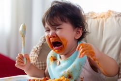 Wayward little toddler child or infant baby crying that don't want eating food on baby chair Cute infant children get hungry and want new food Children get dirty Kid get tantrum Baby is stubborn baby