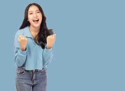 Excited young asian female with raised hands celebrating success Portrait cheerful positive asian woman with raised hands and fists open mouth Girl get happy Pastel blue background, copy space