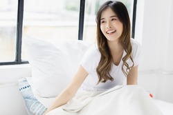 Portrait young beautiful asian woman relax on bed at bedroom Smile happy asian girl look up to copy space Beauty girl sit on bed in morning with smile face She get night enough sleep wake up feel good