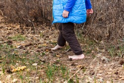 a small child goes barefoot on dry grass and leaves in the forest in spring