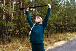 an elderly woman is doing exercises in the woods. Nordic walking poles