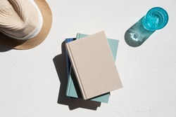 Flat lay of sun hat with a stack of books and a glass of water