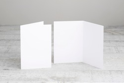Two white greeting cards mockup, standing upright on a white wooden desk. Blank, open and closed cards template. 