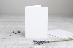 One white greeting card mockup, standing upright on a white wooden desk. Blank, closed card template with envelope. 