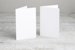 Two white greeting cards mockup, standing upright on a white wooden desk. Blank, closed cards template. 