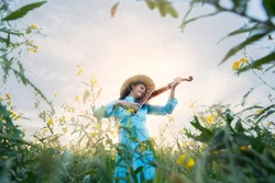 Vietnamese girl playing music from the violin in the middle of a vast meadow.