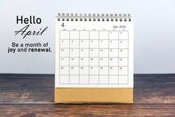 April 2022 calendar on wooden rustic table with hope and positive text message- Hello April. Be a month of joy and renewal. Welcome month of April 2022.