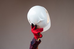 White construction helmet close-up. The man makes a greeting gesture with a white construction helmet. A gloved hand raises the helmet above his head.