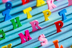 Large multi-colored letters of the English alphabet. The Latin letters cast a shadow on the blue table. The background of English letters is blurred at the edges. The concept of learning and literacy.