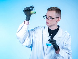 Portrait of a chemist with two test tubes in his hands. He looks at one of them. Young scientist chemist. Chemist student is engaged in national research. Chemical laboratory employee.