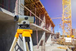 Geodesy. Theodolite at a construction site. Surveyor secured the level to a tripod. Construction crane near the house. Concept - geodetic surveys. Concept - work as a surveyor. Topography.