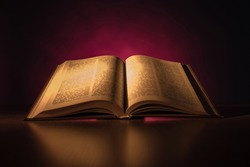 Book emitting light on a dark background. An open book is reflected in table. Book as a symbol of bible. Concept - reading christian literature. Open bible with text close-up. Bible with blurry text