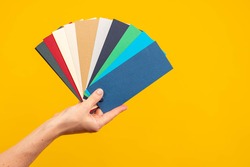 Fan of palette. Color scheme in female hands. Female hand with multi-colored cards. concept is choice of color. Fan palette in hand of designer. Multi-colored palette on yellow background.