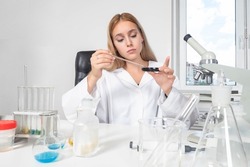 Biologist at work steel. Chemist next to microscope. Woman chemist. Female employee of chemical laboratory. Young girl works in laboratory. Portrait of laboratory technician. Biologist in white coat