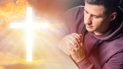 Praying Christian. Praying man closed his eyes. He crossed his palms for prayer. Glowing Christian cross in sky. Catholic cross. Close-up portrait of Catholic. Catholic prayer. Prayer to god