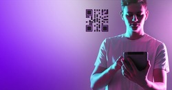 QR code in portable tablet. Technological image on purple neon background. Tablet in hand of man. QR code near man. Scan QR key. Concept of authorization using bar code. Quick Response code. 