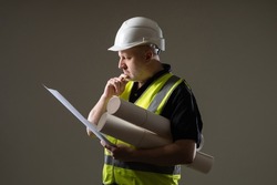 Portrait engineer-architect with blueprints in his hands. Architect in construction uniform. Construction engineer on dark background. Builder was thinking about something. Man engineer with papers