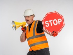 Hazard warning. Builder demonstrate stop sign. Road worker tries to stop. Man in orange vest shows stop sign. Road worker shouts into megaphone. Concept of ban on passage due to danger