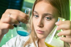 Chemist girl portrait. Chemist girl face. Chemist with two test tubes. Chemistry, research, experiments, tests. Woman examines chemical liquids in flasks. Chemistry teacher demonstrates experiments.