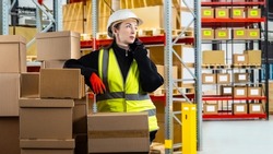 Postal warehouse worker. Woman with phone. Woman works in warehouse for postal company. Cardboard parcels in front of girl with phone. Postal worker is talking on phone. Female in yellow vest