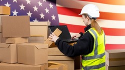 Woman with boxes and laptop. USA customs check concept. Customs officer woman. Girl with computer in front American flag. Lady in yellow vest with her back to camera. Customs clearance goods from USA