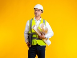 Indian builder. Man builder with blueprints in his hands. Construction company employee with laptop. Guy in construction vest. Businessman in clothes for construction site. Man builder on yellow