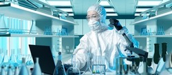 Scientist in chemical laboratory. Woman Chemist in protective suit. Scientist with laptop and laboratory flask. Girl is sitting at laboratory table. Scientific experiments in chemistry. 